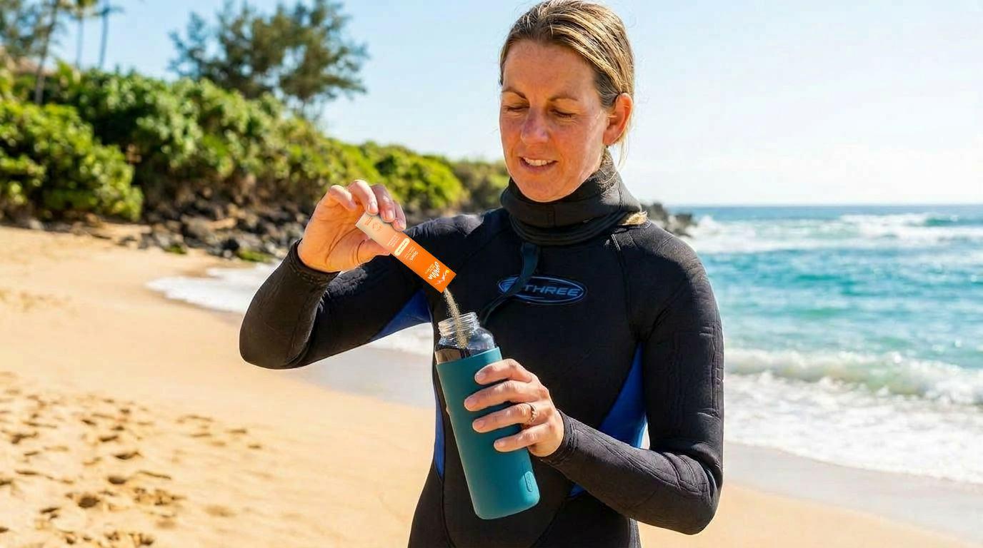 A woman in a wetsuit tearing a Yama stick open and pouring it into a bottle on the beach