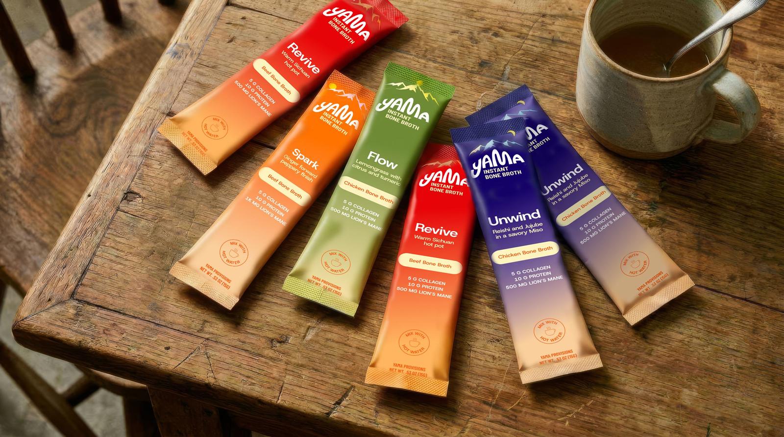 The four Yama stick packs laid across a wooden table beside a mug of hot bone broth